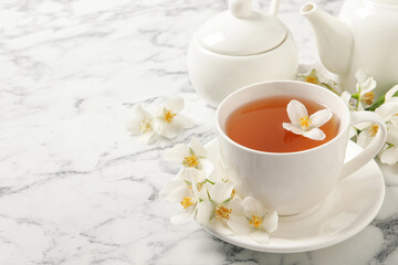 Obraz na płótnie Canvas Aromatic jasmine tea and fresh flowers on white marble table, space for text