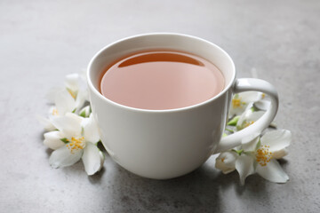 Cup of aromatic jasmine tea and fresh flowers on grey table