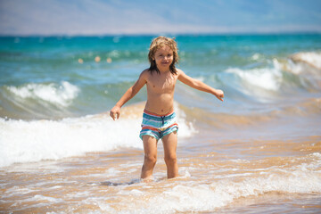 Fototapeta na wymiar Child boy on the coast. Little kid playing in the ocean. Holidays on the sea. The child in waves.