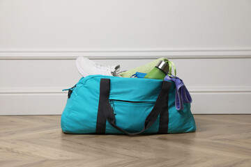 Blue gym bag with sports accessories on floor near white wall indoors