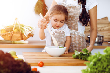 Happy woman and her daughter making healthy vegan salad and snacks for family feasting in sunny kitchen. Christmas, New year, Thanksgiving, Anniversary, Mothers Day. Healthy meal cooking concept