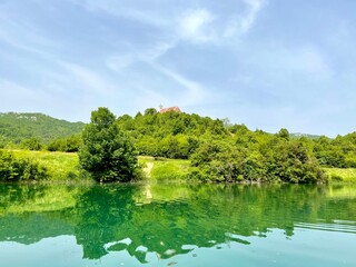 KOSINJ, CROATIA, June 2021 - Beautiful Lika river riverscape. Reflection in water and dramatic sky. Small church in distance on the top of the hill