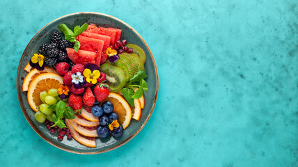 Delicious healthy salad of fresh fruits, berries and edible flowers on plate. Clean eating. Top...