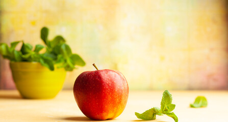 Still life with red apple and fresh mint in bowl on yellow background. Front view, copy space.
