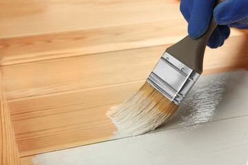 Worker applying white paint onto wooden surface, closeup. Space for text