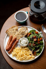 Full english breakfast with scrambled eggs, toast and sausages served with a cup of green tea, dark atmospheric photo