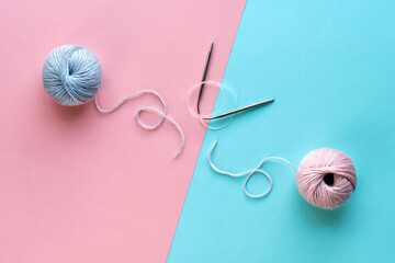 Wool yarn balls and knitting needles with string on split pink and mint blue paper background....