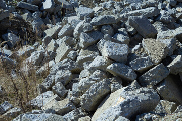 A pile of piled, gray, debris of concrete slabs and stones among the yellow, dry grass close-up....