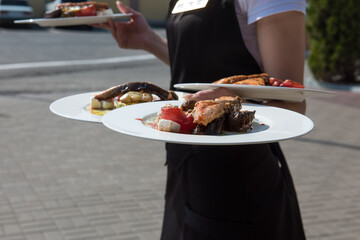 Dishes with roasted trout with vegetables in hands of waitress