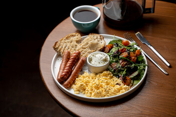 Full english breakfast with scrambled eggs, toast and sausages served with a cup of green tea, dark atmospheric photo