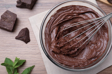 Whipping chocolate cream with balloon whisk on wooden table, flat lay