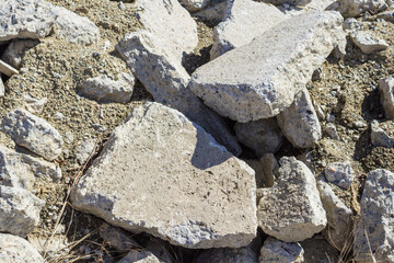 A pile of piled, gray, debris of concrete slabs and stones among the yellow, dry grass close-up. Landfill for construction waste. Traces of an earthquake and a devastating catastrophe.  Desolate area.