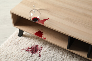 Overturned glass and spilled red wine on white carpet indoors