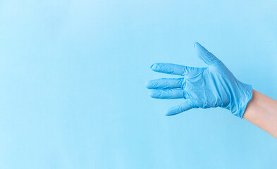 Human hand wear blue nitrile disposable glove above light blue background. Safety first concept.