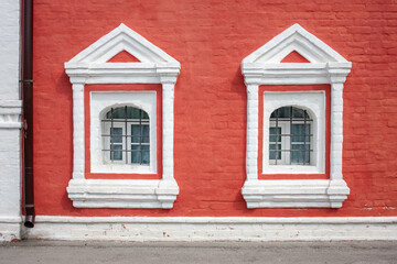 Two windows on the red wall of the house. Decor and framing of window openings on the facade. Window openings with a semicircular arched finish, included in a rectangular frame.