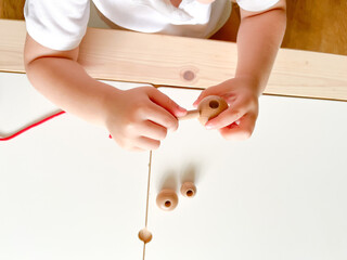 A child puts beads on a red rope. The development of fine motor skills, preschool education, the Montessori method. Lesson with the kid. Smart child. View from above. Nursery and kindergarten concept.