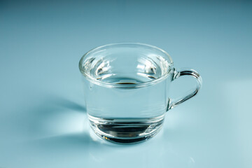 A glass of clear water, Minimal layout, Light reflection, Shadow play. Pastel blue background