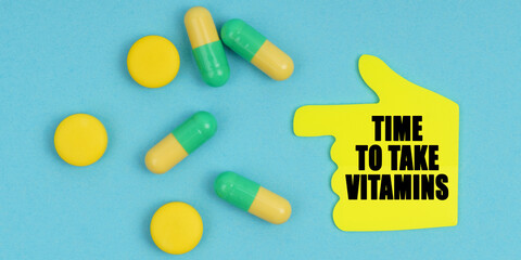 On a blue background, there are pills and a hand-sticker with the inscription - Time to take vitamins