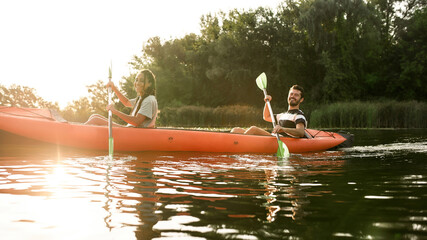 Smiling young couple kayaking in a river surrounded by the beautiful nature on a summer day