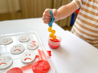 The study of emotional intelligence. Children's emotions. Children's hands with yellow and red emoticons. Montessori concept. The child draws with paints. Fine motor skills. Children's experiences.