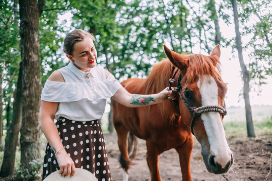 photo of a young smiling blonde, in a white blouse and skirt, with a horse, in a summer forest