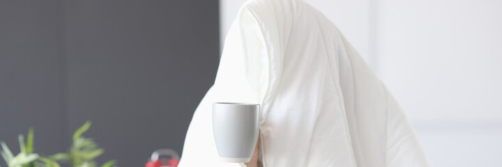 Man sitting under blanket with cup of coffee
