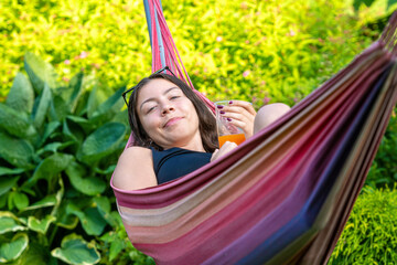 gorgeous girl lying on the hammock relaxing and drinking orange juice