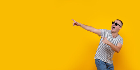 Fototapeta na wymiar Portrait of funny young man in casual clothes pointing index fingers aside up isolated on yellow orange wall background in studio. People sincere emotions lifestyle concept. Mock up copy space