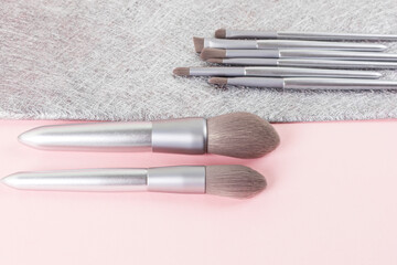 Set of silver color professional makeup brushes on pink and gray colored composed background. Creative concept of beauty. Copy space. Close up.