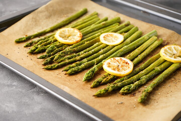Fried asparagus and lemon on a baking sheet.