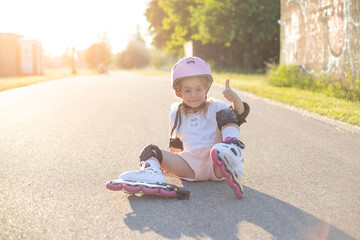 Portrait of little girl in roller skates, sitting on ground.