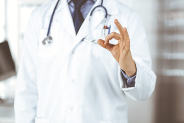 Unknown male doctor standing straight with OK sign in clinic near his working place, closeup. Perfect medical service in hospital. Medicine and healthcare concept