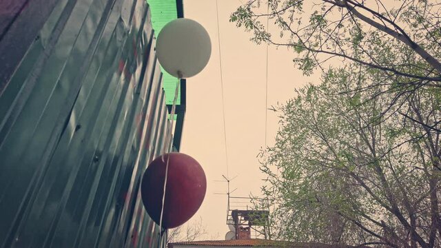 Depression, party is over. Red and white balloons set near trash dumpsters of a ghetto.