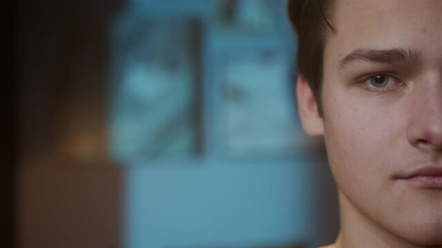 Half-face portrait of young sad man with light blue eyes, looking in camera with joyless, sorrowful view. Close-up of male face student.