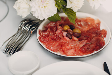 Various cold cuts on a plate with white flowers on table.