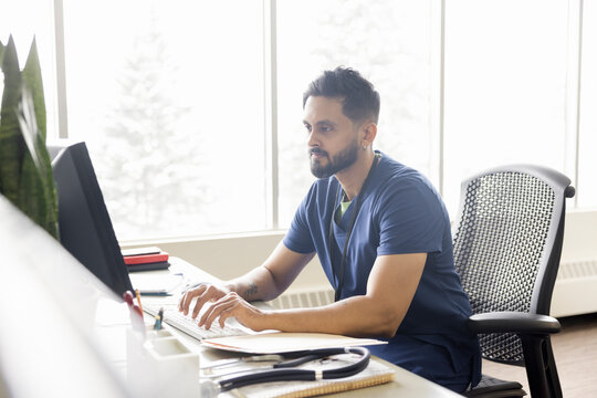 Male Nurse Working At Computer In Clinic Office