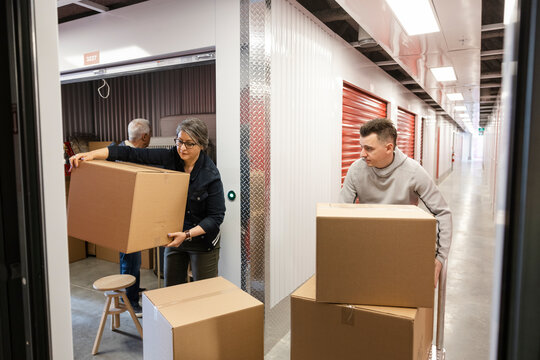 Son Helping Senior Parents Move Boxes Into Storage Facility Locker