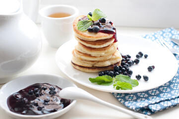 Breakfast with tea, pancakes, fresh blueberries and mint. Fried pancakes on a white plate.
