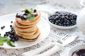 Breakfast with tea, pancakes, fresh blackberries and mint. Fried pancakes on a white plate.