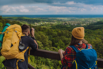 Young couple of hikers standing on a lookout and using binoculars while spending day in the nature