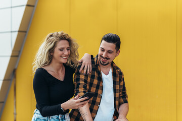 Young beautiful couple using smartphone while holding a shopping cart
