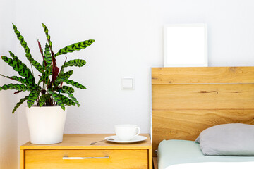wooden bedside table with Calathea in a flowerpot, tea or coffee cup on a saucer, head of the...