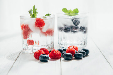 Summer drinks. Refreshing water or soda with ice and berries in a beautiful glass stands on a white wooden table. Seasonal drinks and cocktails