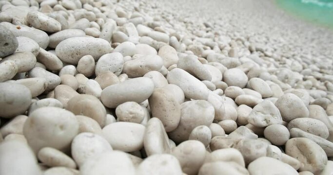 Close up shot of white pebbles and blue sea waves crushing on background, 4K beach background video.