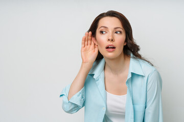 A young woman eavesdrops on someone else's conversation with her hand to her ear. The concept of...