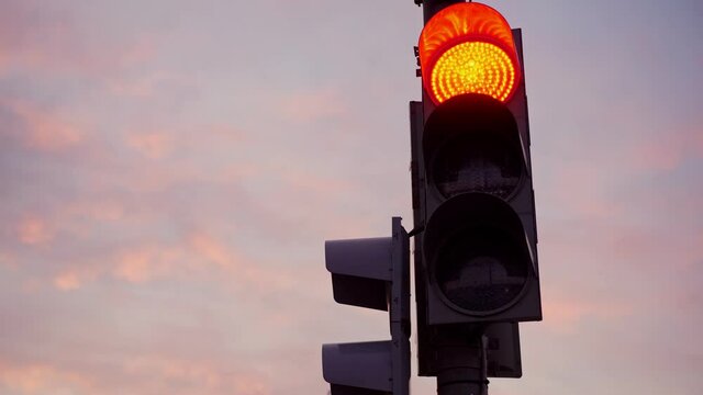 Cinematic hand-held shot. A close-up of a red traffic light turns green against a sunset sky.