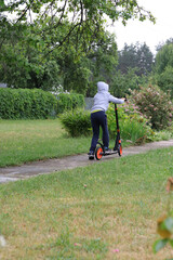 Child riding a scooter on a concrete path in the park