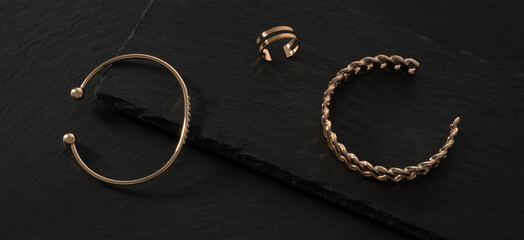 Panoramic shot of modern bracelets and double shape ring on black stone trays with copy space