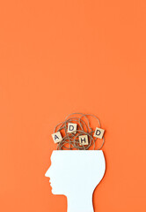 Silhouette of human head and wooden blocks with the letters ADHD on orange background. Minimal concept of attention deficit hyperactivity disorder. Vertical banner, place for text - obrazy, fototapety, plakaty