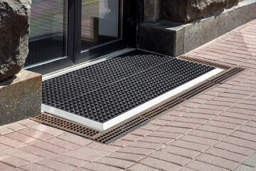 entrance to the store from a pedestrian sidewalk from a rubber foot mat with storm drain mesh, the facade of the exterior of a building close-up in sunny dry weather side view nobody. - obrazy, fototapety, plakaty
